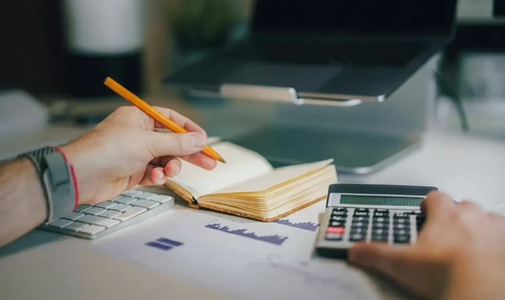 A person sitting at a desk with a notebook, calculator and a pencil
