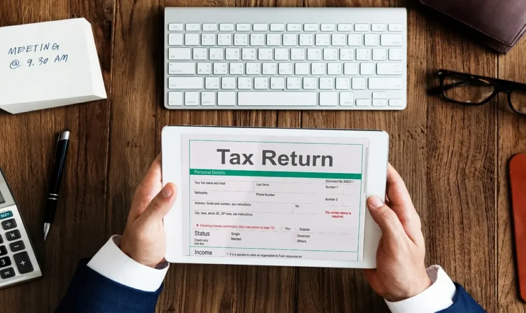 Person holding tax returns form with white keyboard on a wooden table